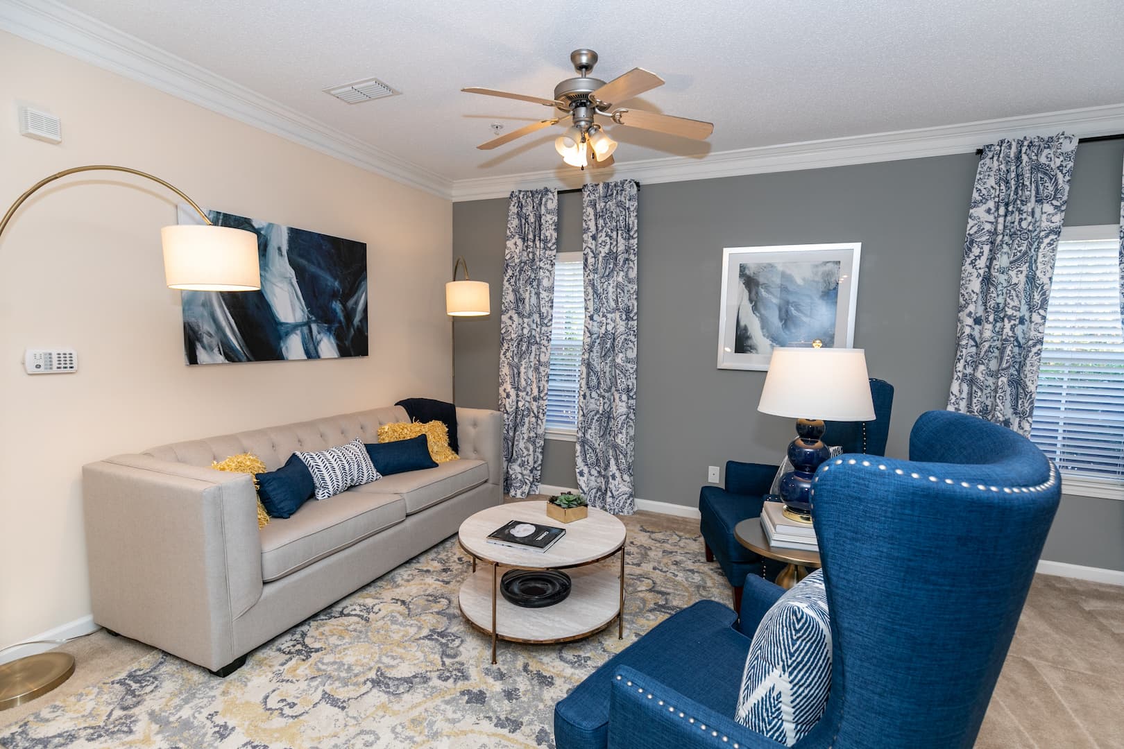 model living room with ample lighting, ceiling fan and crown molding