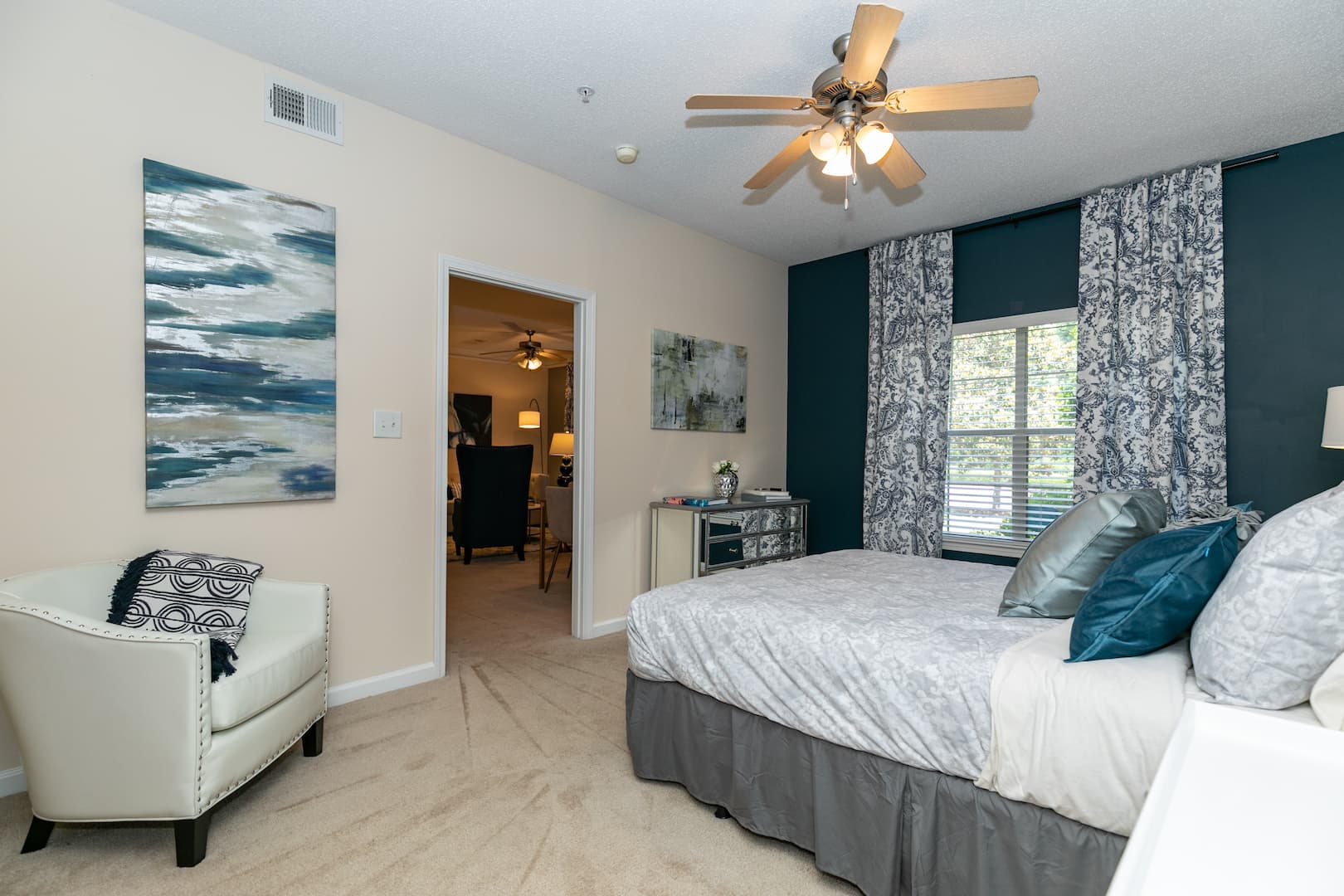 model carpeted bedroom with ceiling fan, and leading to living area