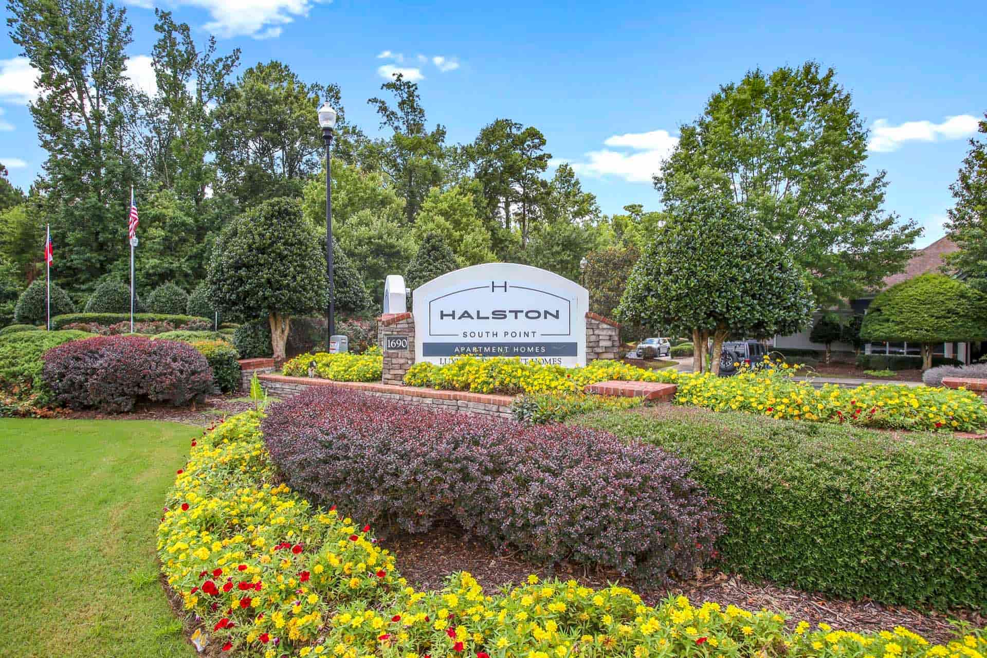 Halston South Point apartment homes sign in bush and flower bed