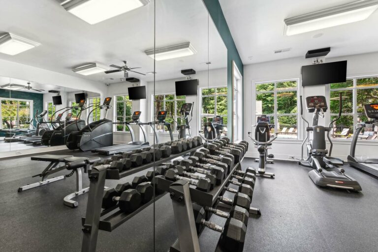 Fitness center with weight equiptment, treadmills, elliptical, excercise bike and stair amster with ceiling fan and two tvs on the wall.