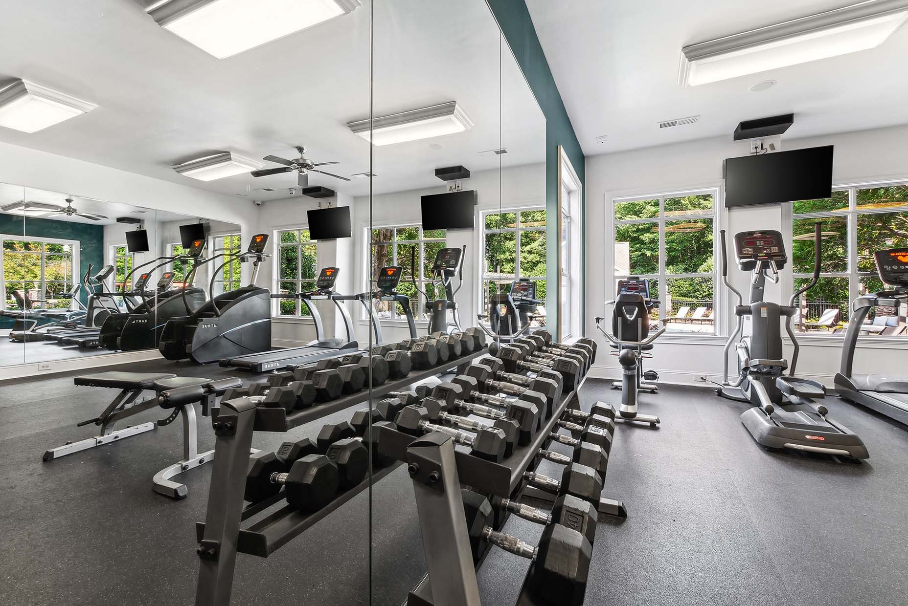 Fitness center with weight equiptment, treadmills, elliptical, excercise bike and stair amster with ceiling fan and two tvs on the wall.