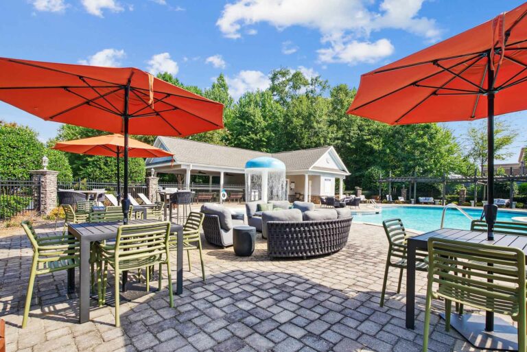 Outdoor lounge containing seating areas and tables with chairs and umbrellas on the sun deck with pool and splash zone in the background.